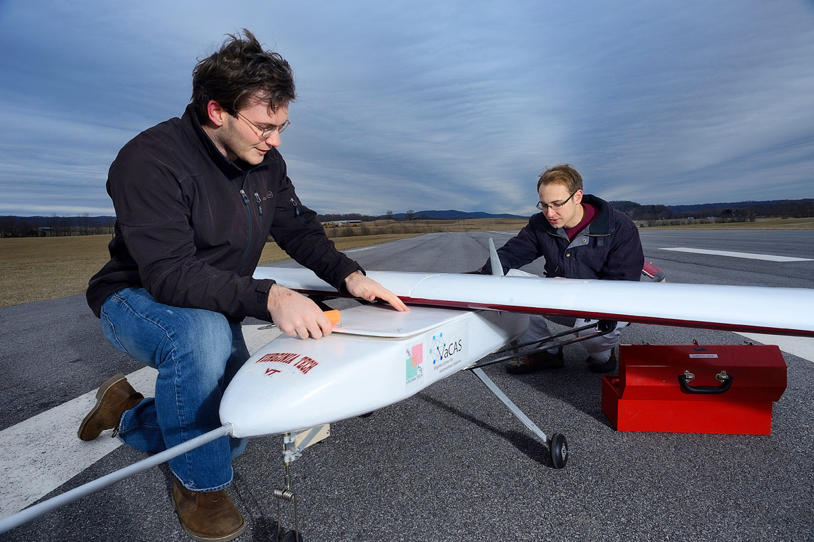 Students work on a remote control airplane on a runway.