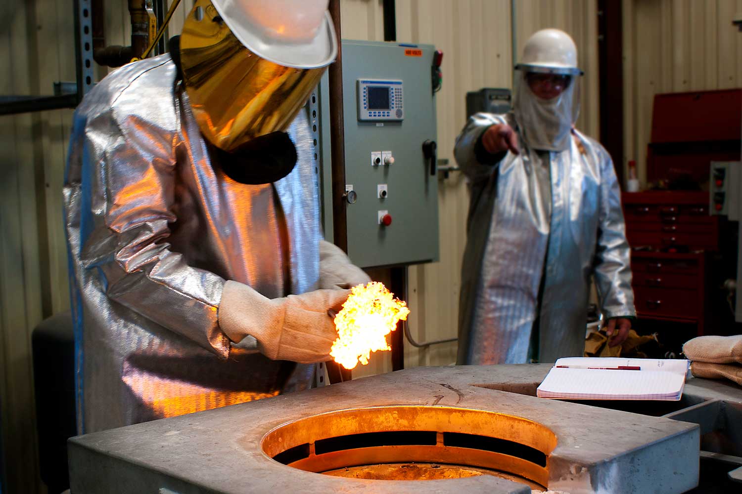 A Material Science student works with molten material in a lab and is wearing a fire suit.
